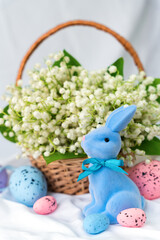Festive composition with Easter Bunny, decorative eggs and a basket of lilies of the valley. Selective focus.