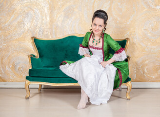 Beautiful smiling sensual woman in rococo style medieval dress sitting in the sofa