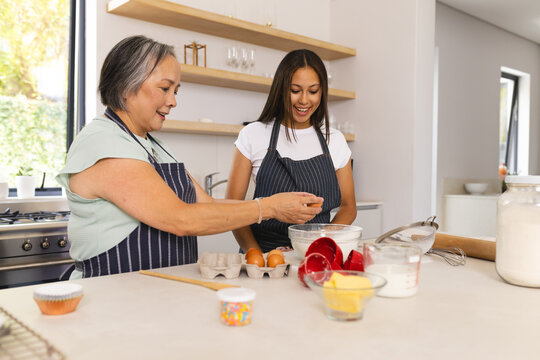 Asian grandmother and biracial teenage granddaughter are baking together in the kitchen at home