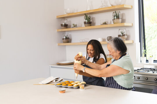 Asian grandmother and biracial teenage granddaughter are baking together at home with copy space