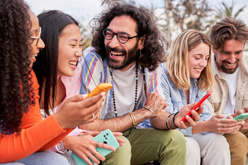 Happy multicultural group of friends sitting outside using cellphones, gathered to have fun...