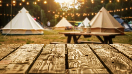 A wooden table overlooking the tents and several picnic tables. The tents are illuminated with lights, creating a warm and cozy atmosphere. Camping concept.