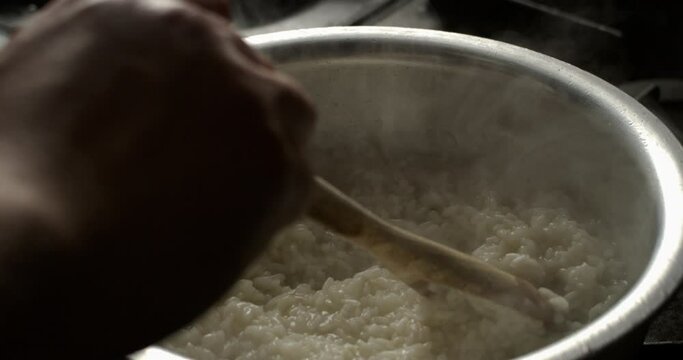 Super slow motion close up of professional chef is mixing with wooden spoon boiled white rice in pot while preparing Italian dish of risotto with vegetables sauce in kitchen of restaurant at 1000 fps.