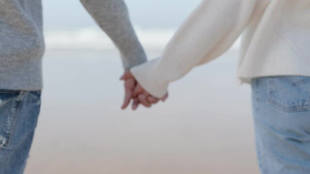 A close-up image depicting the hands of a young man and woman reaching out to each other near the ocean, symbolizing connection and support.