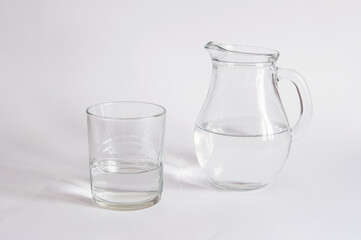 A  jug and a crystal glass containing water, isolated on a white background