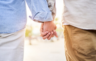 Beautiful close up photo of an unrecognizable caucasian couple holding hands outside against the sunlight. Copy space. - obrazy, fototapety, plakaty