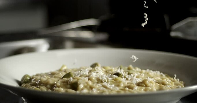 Super slow motion macro of professional chef grating parmesan cheese on traditional Italian dish of rice risotto with sauce and vegetables in plate ready to be served to customer at restaurant kitchen