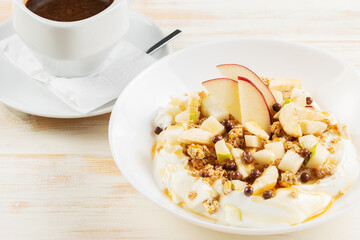 Yogurt with flakes, fruits and cup of coffee on white wooden background. Βreakfast concept.