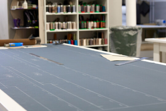 On the cutting table there is a gray fabric for the pattern. In the workshop at the garment factory, a fabric with a traced pattern is laid out on the table - Powered by Adobe