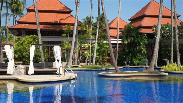 Luxurious tropical resort with inviting swimming pool and modern cabanas surrounded by lush palm trees. Vacation and travel in exotic destination.