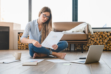Young businesswoman working with charts and documents sitting at home on the floor. Freelancer...