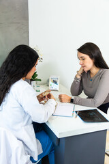 Female hispanic patient or student paying attention to explanation of latin dentist holding a plastic denture model in a dental office desk.