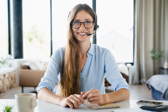 Young female IT support manager wearing headphones consulting customers online. Videocall with sales manager teleworking and looking at the camera