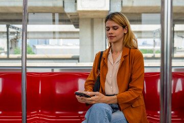 A young woman in casual attire is focused on her smartphone while riding on a modern subway train.