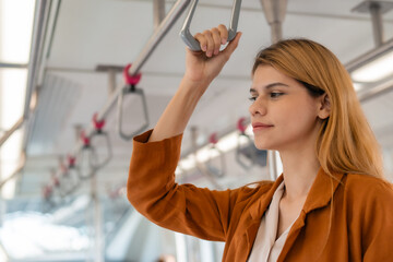 A woman traveling on public transport holds onto a handrail on a train. It symbolizes safety and...