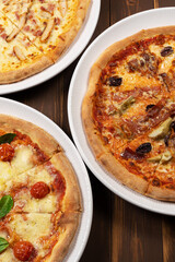 Three different pizzas on wooden background with tomato sauce, mixed cheese selection, ham and pork gyros.