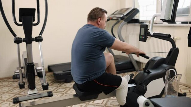 prosthetic equipment, Limb training, Gym exercise. Man with artificial limb is using rowing machine at gym.