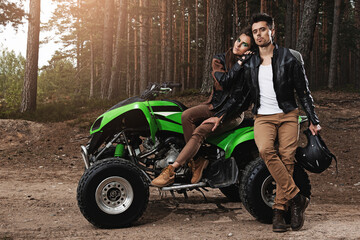 Naklejka premium Stylish man and woman in leather jackets pose with a green ATV in the forest