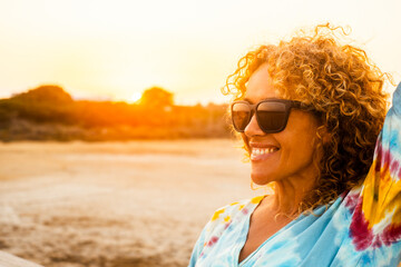 Sunny outdoor portrait of curly young woman smiling and wearing sunglasses with sunset backlight....