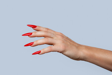 Closeup of  elegant female hand with red stiletto nails on gray background
