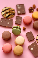 Pastel macarons, almond chocolate, peanut butter cookies and various nuts on bright pink background. Selective focus.