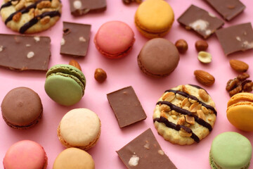 Pastel macarons, almond chocolate, peanut butter cookies and various nuts on bright pink background. Selective focus.