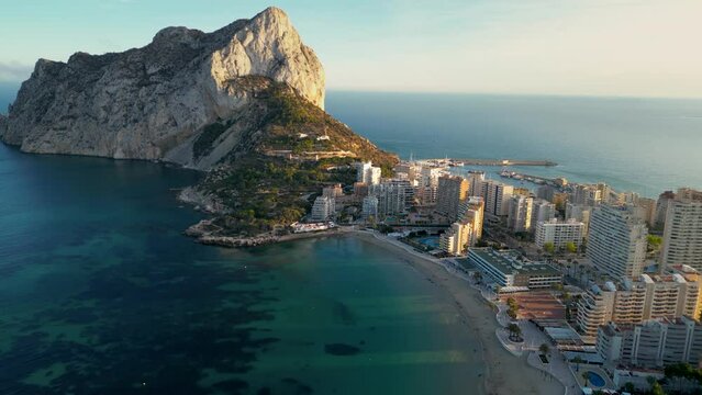 Aerial drone view of Calpe city at sunset. Warm colours reflecting on Penon de Ifach Mountain and buildings. Famous travel destination in province of Alicante, Valencian Community, Spain. Forward 