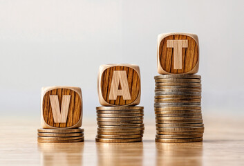 Stacks of coins with wooden blocks spelling out text word VAT on top of each stack - obrazy, fototapety, plakaty