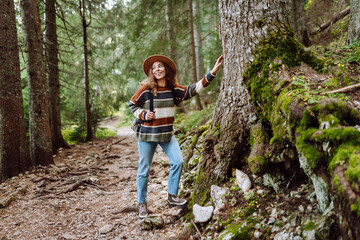 Naklejka na ściany i meble Young woman - tourist walks along a hiking trail against the backdrop of mountain scenery. Adventure, travel, tourism.