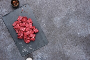 Sliced raw beef meat for slices for the preparation of goulash, stew on a shaleboard on a black...