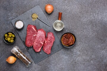 Prepared ingredients for cooking stewed beef with dried tomatoes and olives on a black concrete background.