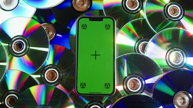Smartphone with chroma key screen among cd disks close-up. Green screen on mobile phone lays on dvd disk background