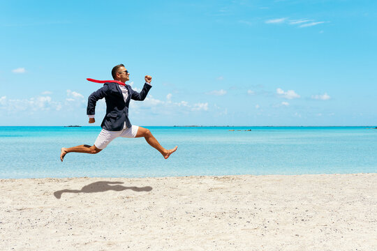 Happy businessman running away from office work on the beach.