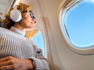 One female people travel on board airplane sitting on seat and looking outside the window wearing...