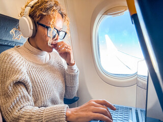 Middle aged business woman working on laptop while sitting on airplane. Travel and business trip lifestyle female people using computer and looking outside the window