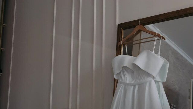 women's wedding dress hangs near the window in which the forest is reflected	