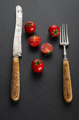Ripe cherry tomatoes with vintage fork and  table-knife on black background