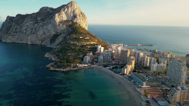 Beautiful sunset over Calpe city and Pe&ntilde;&oacute;n de Ifach mountain. Drone backwards and panning right. Sunset colours reflecting on buildings and mountain. Travel destination in Spain, Alicante Province.