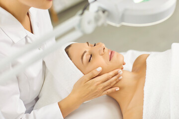 Young professional woman cosmetologist doing skin care facial treatment examining its condition for...
