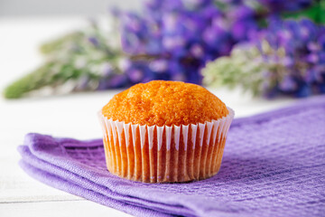 Freshly baked muffins and purple lupins on white wooden background.