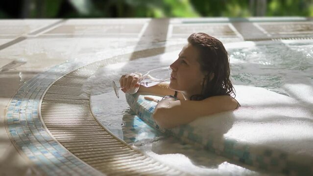 Young woman drink sparkling wine and relaxes in the hot tub
