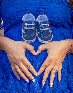 Persona embarazada con vestido azul, zapatos de bebe y formando un corazón con las manos