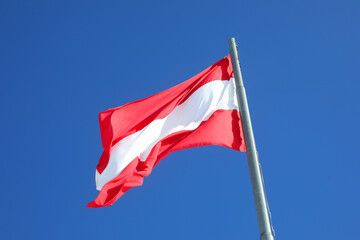 Austrian flag in white and red colors waving against a blue sky - 785641479
