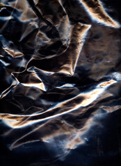 Creased surface. Crumpled material. Black color metallic overlay light refraction wrapped foil worn aged film glow texture grunge abstract background.