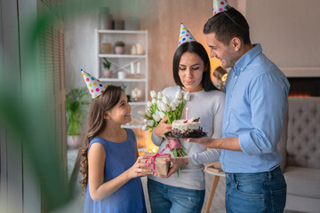 Happy family celebrating mother's birthday. Man standing with holiday cake in hand, little girl...