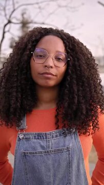 Vertical portrait of a confident African woman looking at camera with a serious face while standing outdoors. BLM.
