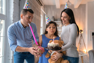 Young father and mother celebrating birthday of their daughter. Family wearing party hats and...