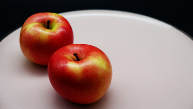 Two apples on a pink plate with a black background. The beautiful apples with still-life concept. Healthy and organic fruit. Close-up image of red apple texture, selective focus, and copy space.