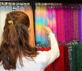 girl while choosing a red necklace of glass beads among many colorful necklaces in the shop - 785647253