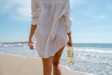 Young woman holds bottle of white wine and glasses on a sunny beach